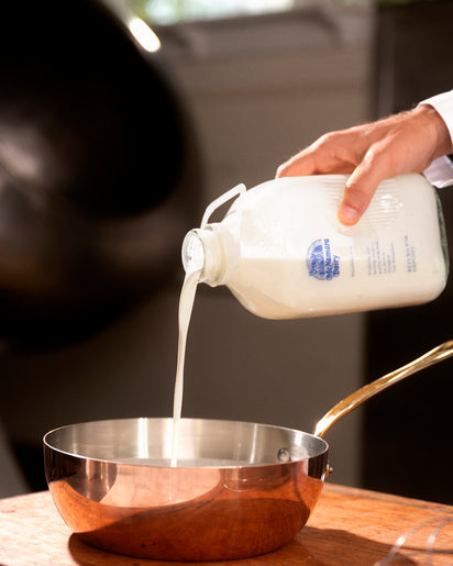 Person pouring milk from a container into a pan with a blurred background