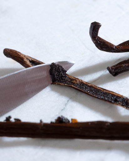 Vanilla beans being sliced with a knife on a white background