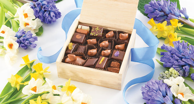 Wooden box of assorted chocolate bonbons surrounded by spring blue yellow and white flowers