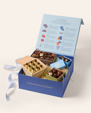 An open blue box with an assortment of gourmet chocolates (chocolate mice, Snowmen, penguins and assorted shapes). The main box is navy blue the inside of the open lid depicts rows of colorful illustrations and text.