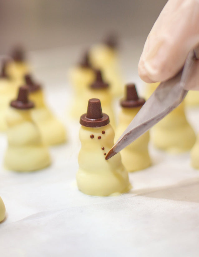 Chocolate buttons being hand-applied onto a Chocolate Snowman by one of our chocolatiers.