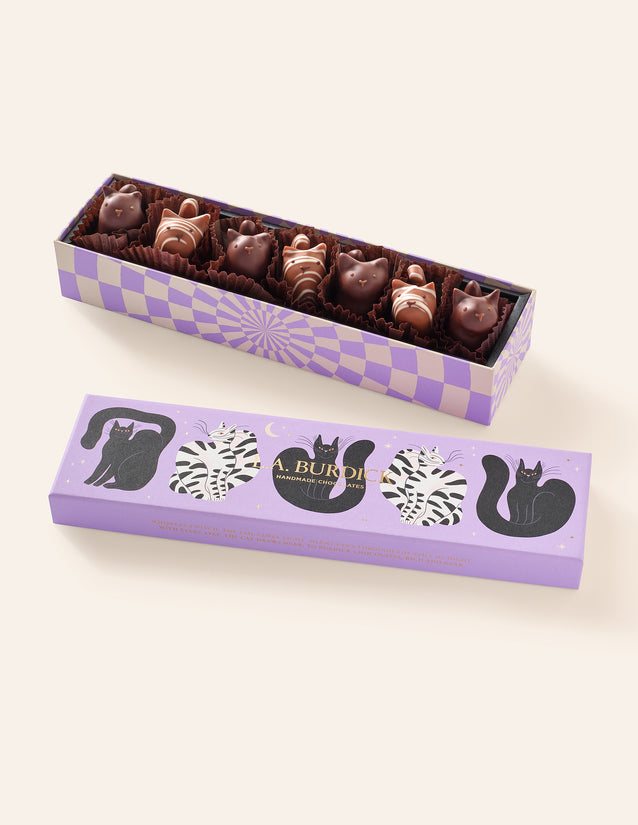 Seven Chocolate Cats (four dark chocolate, and three striped milk chocolate) nestled inside their purple gift box with illustrated cats on the lid.