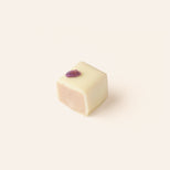 Square piece of white chocolate, cut in half to show the interior, with a purple candied violet on a light beige background