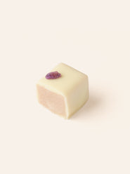 Square piece of white chocolate, cut in half to show the interior, with a purple candied violet on a light beige background
