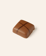Square piece of artisan milk chocolate with a dark chocolate cross pattern on top, set against a plain light background.