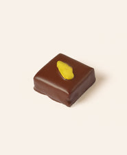 Square dark chocolate bonbon with a slice of pistachio on the top