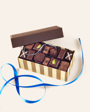 A box of assorted chocolate bonbons including a dark chocolate mouse  with a blue silk tail. Below the box is a blue ribbon. 