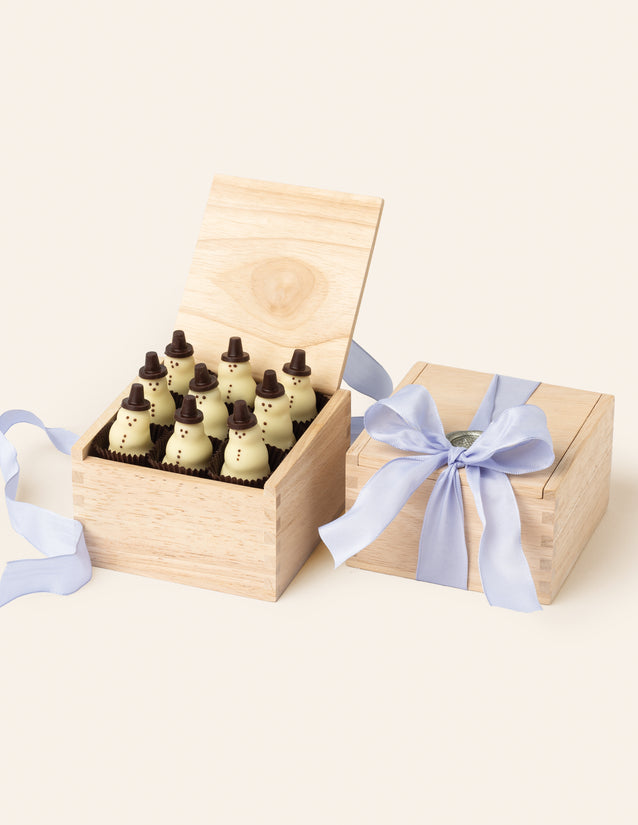 Nine charming Chocolate Snowmen with chocolate top hats, shown inside a wooden box and finished with a periwinkle ribbon.