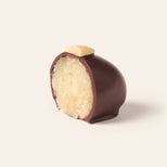 Chocolate covered marzipan egg cut in half to show the interior, topped with an almond sliver on a cream background