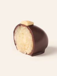 Chocolate covered marzipan egg cut in half to show the interior, topped with an almond sliver on a cream background