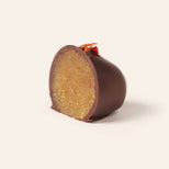 Chocolate covered marzipan carrot egg cut in half to show the interior, topped with a dried carrot piece on a cream background