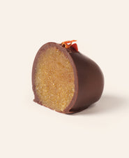 Chocolate covered marzipan carrot egg cut in half to show the interior, topped with a dried carrot piece on a cream background
