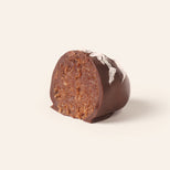 Chocolate covered chocolate marzipan egg cut in half to show the interior, topped with coconut flakes, on a cream background