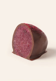 Chocolate covered marzipan egg cut in half to show the interior red raspberry marzipan filling