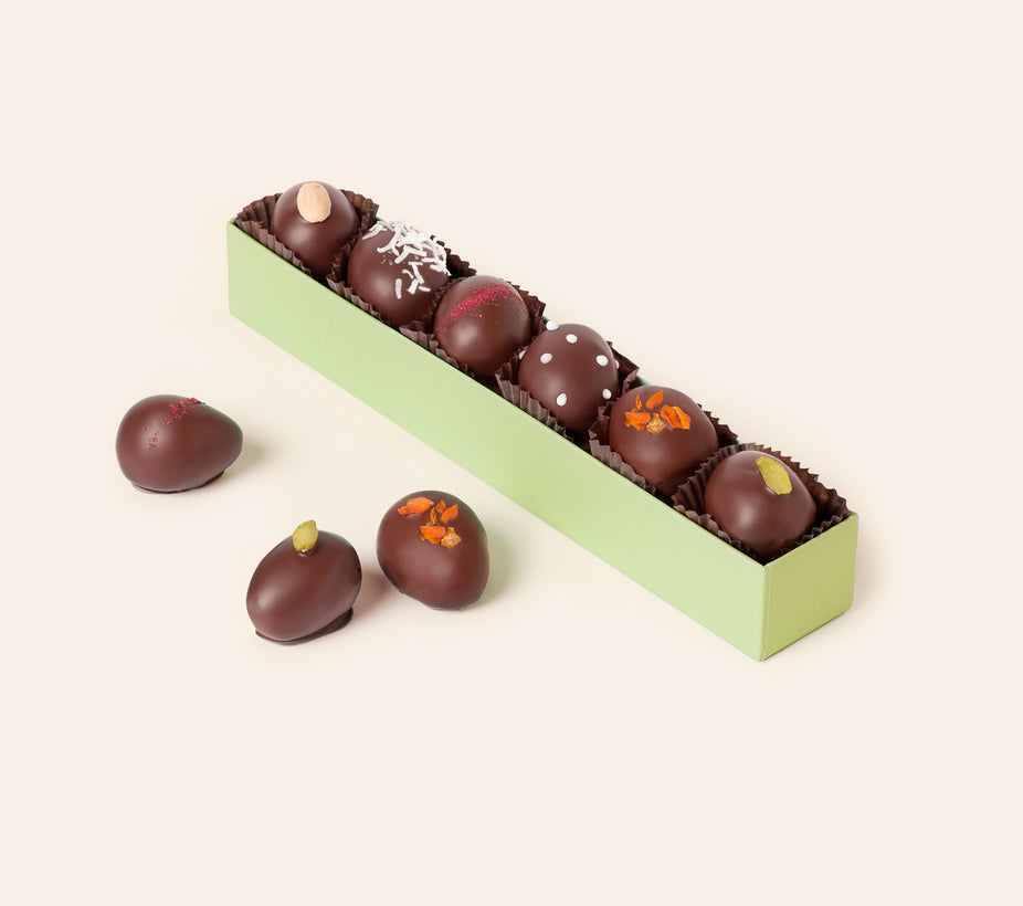 Six dark chocolate–enrobed marzipan eggs with assorted garnishes in a long green gift box