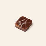Chocolate bonbon with a white drizzle on a light beige background