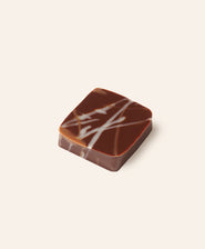 Chocolate bonbon with a white drizzle on a light beige background