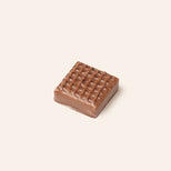 Square milk chocolate bonbon with a grid pattern on a light beige background
