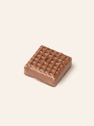 Square milk chocolate bonbon with a grid pattern on a light beige background