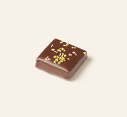 Chocolate square bonbon with pistachio bits on a light beige background