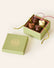 Four chocolate mice, dark chocolate, milk chocolate and white chocolate, with silken green and pink tails, in a square green box. The lid of the box is embossed with a gold foil L.A. Burdick logomark.