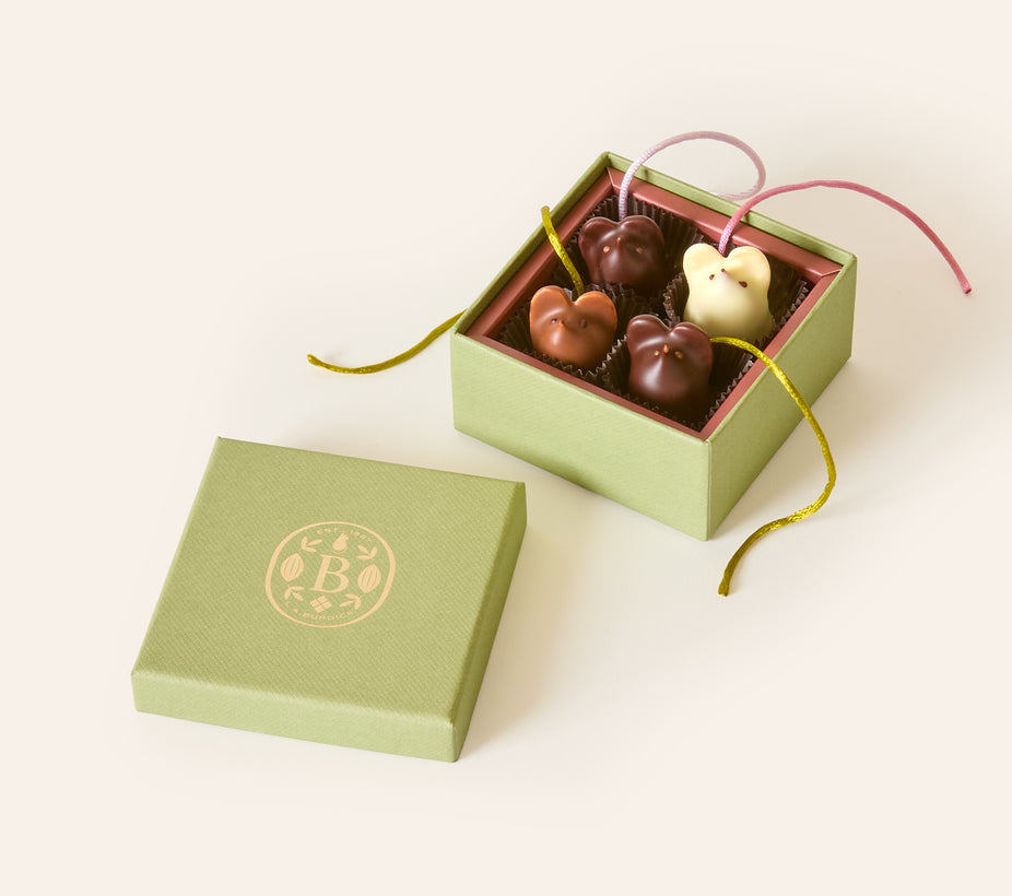 Four chocolate mice, dark chocolate, milk chocolate and white chocolate, with silken green and pink tails, in a square green box. The lid of the box is embossed with a gold foil L.A. Burdick logomark.