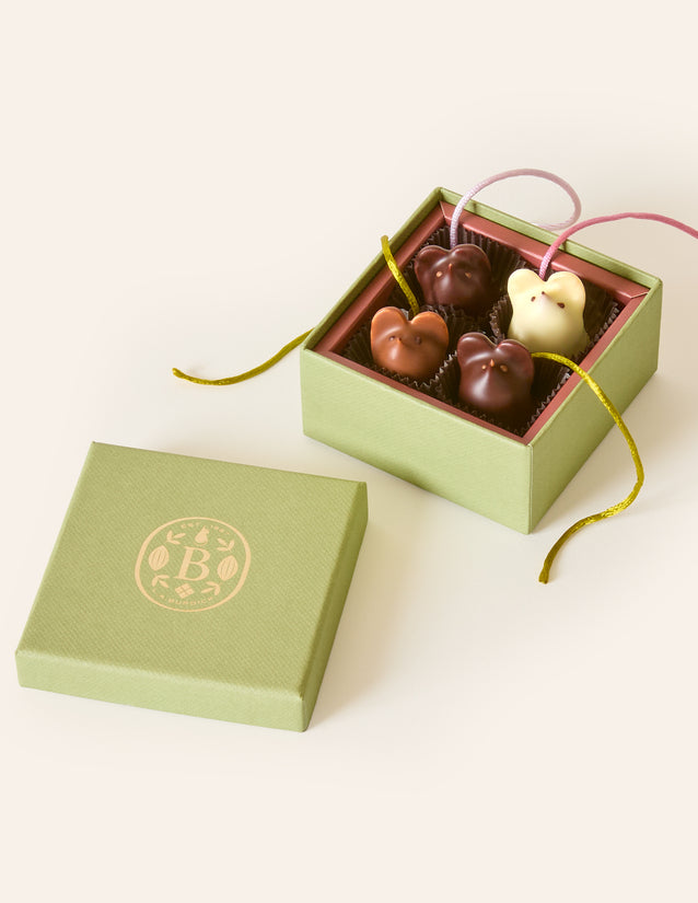 Four chocolate mice, dark chocolate, milk chocolate and white chocolate, with silken green and pink tails, in a square green box. The lid of the box is embossed with a gold foil L.A. Burdick logomark.