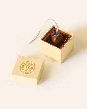Dark chocolate mouse with a light gray silken tail in a square cream box. The lid of the box is embossed with a gold foil L.A. Burdick logomark.