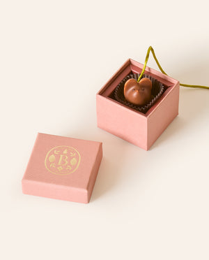 Milk chocolate mouse with a olive green silken tail in a square dusty pink box. The lid of the box is embossed with a gold foil L.A. Burdick logomark.