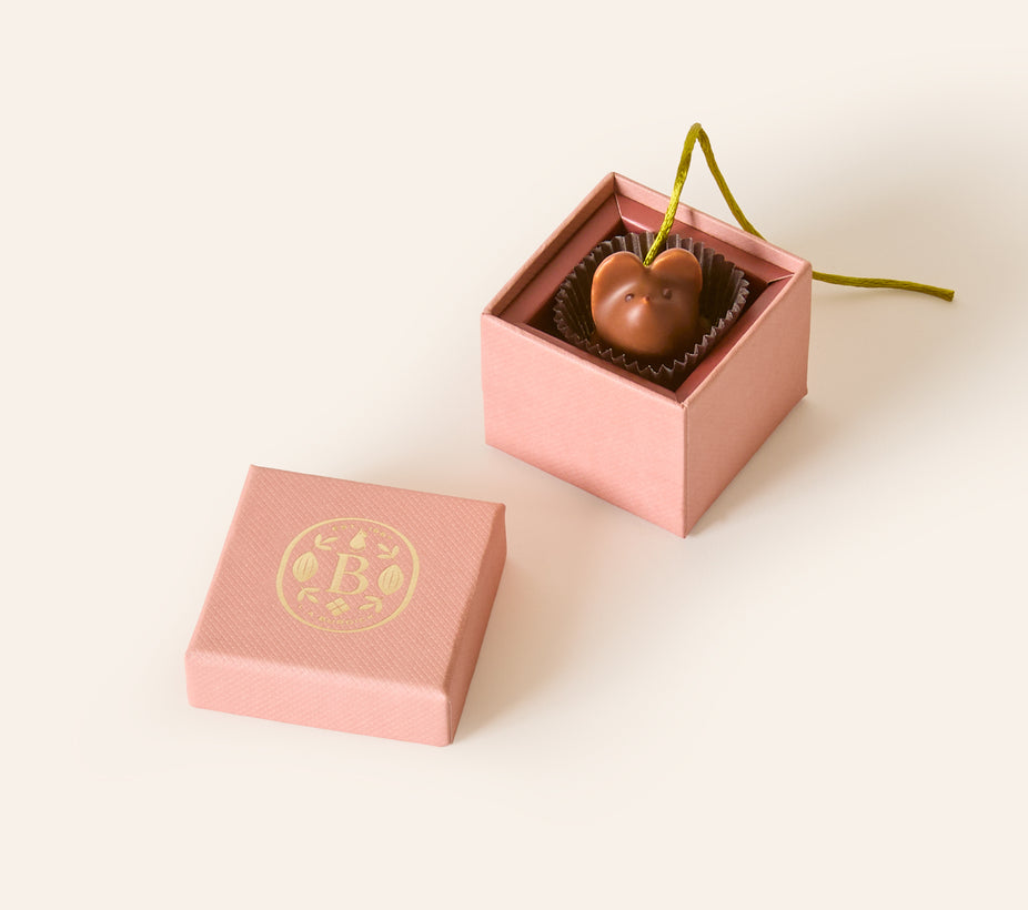 Milk chocolate mouse with a olive green silken tail in a square dusty pink box. The lid of the box is embossed with a gold foil L.A. Burdick logomark.