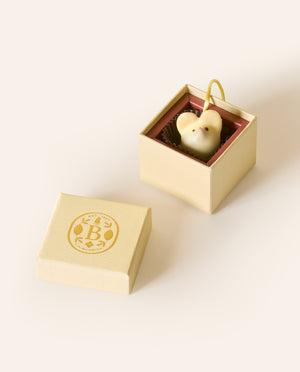 White chocolate mouse with a yellow cream silken tail in a square cream box. The lid of the box is embossed with a gold foil L.A. Burdick logomark.