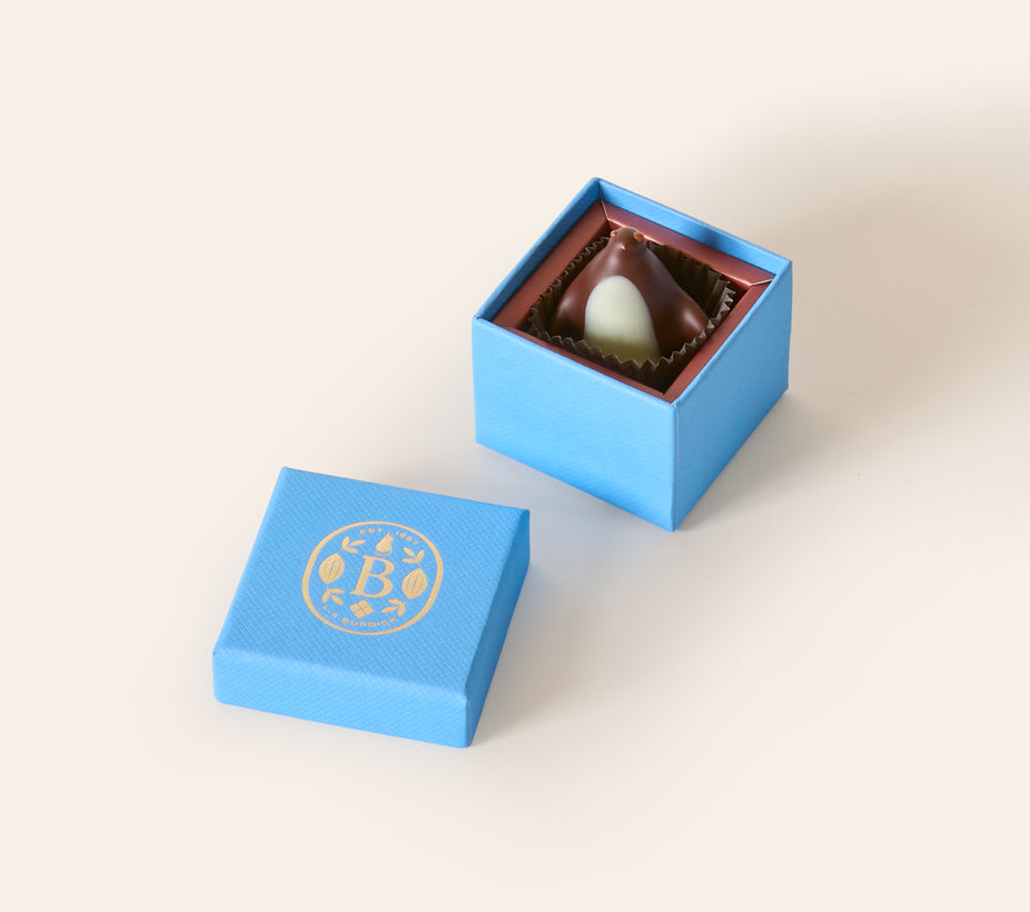 Dark chocolate penguin, with a white chocolate belly in a square light blue box. The lid of the box is embossed with a gold foil L.A. Burdick logomark.