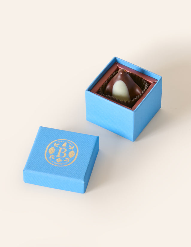 Dark chocolate penguin, with a white chocolate belly in a square light blue box. The lid of the box is embossed with a gold foil L.A. Burdick logomark.