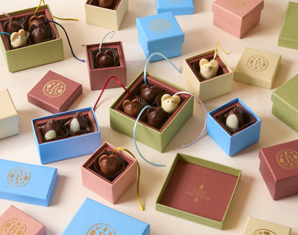 Assorted handmade chocolates shaped like mice, presented in small pastel-colored gift boxes with lids arranged on a light surface.