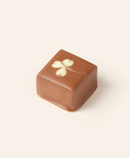 Square milk chocolate bonbon with a four-leaf clover design in white chocolate on a light cream background