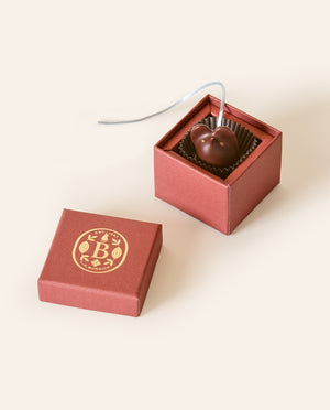 Dark chocolate mouse with a light gray silken tail in a square burgundy box. The lid of the box is embossed with a gold foil L.A. Burdick logomark.