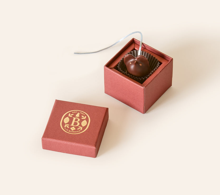 Dark chocolate mouse with a light gray silken tail in a square burgundy box. The lid of the box is embossed with a gold foil L.A. Burdick logomark.